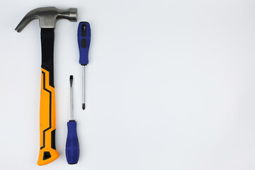 A hammer with an iron base and a yellow-black handle lies on the left, next to it are screwdrivers on a white background with space for text. The concept of repair, hammering. High quality photo