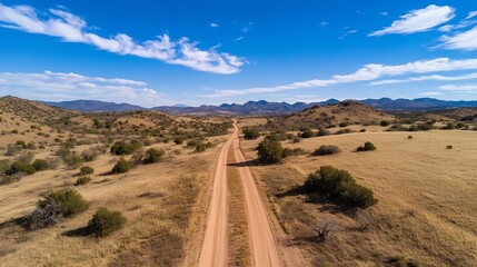 Scenic Aerial View of a Dusty Road Meandering Through Desert Hills Under a Bright Blue Sky : Generative AI