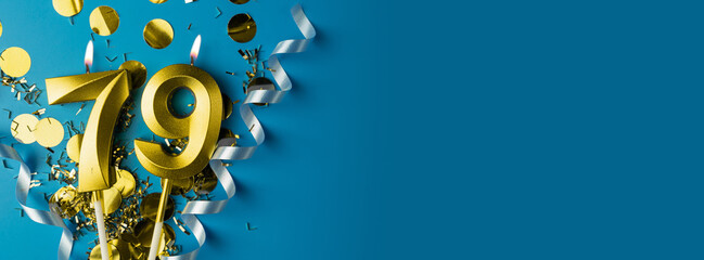 79 years celebration. Gold burning candles of number seventy-nine on blue background with confetti,...