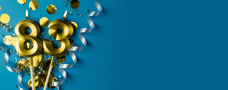 83 years celebration. Gold burning candles of number eighty-three on blue background with confetti, copy space.