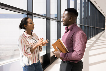 Two African colleagues standing in office hall lead talk, discussing work-related, joint business...