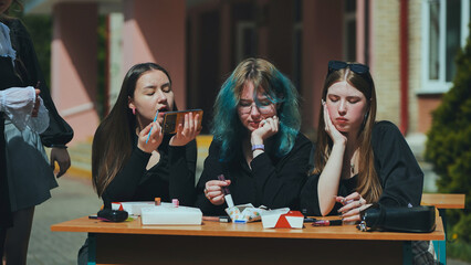 High school girls having a carefree makeup session outdoors during their break, enjoying the sunshine and each other's company