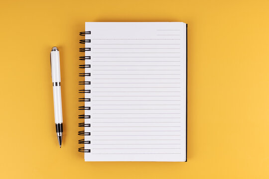 Flat lay view of a notebook and a pen on a yellow background