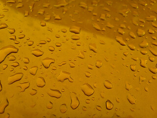 Raindrops on a golden metal surface on a summer day.