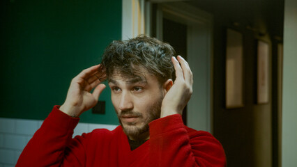 Handsome young man grooming his hair in front of the mirror taking care of his appearance and...