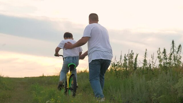Man helping child ride bike. sky cloudy sun setting. happy family, father run holding child bike, childhood bike, childhood dad, dad son, childhood dream riding dad, picnic nature, vacation holiday