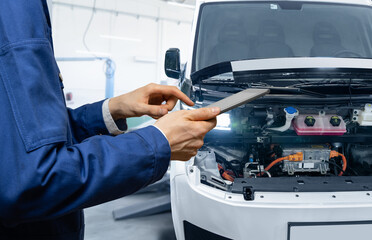 Serviceman with digital tablet next to electric van with open hood. Electric vehicles maintenance © scharfsinn86