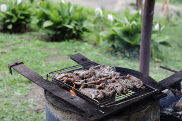 Una toma de cerca de una parrillera casera con varios trozos de carne cocinándose a leña en el campo