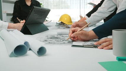 Group of professionals engaged in a collaborative meeting, reviewing blueprints and documents while brainstorming ideas in a contemporary office setting. SACTR