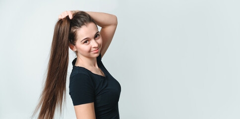 Fototapeta premium Smiling girl of Slavic appearance 20 years old looking at camera isolated on gray background. Black T-shirt. Beautiful brunette with long straight loose hair. Kind friendly look. Without makeup.