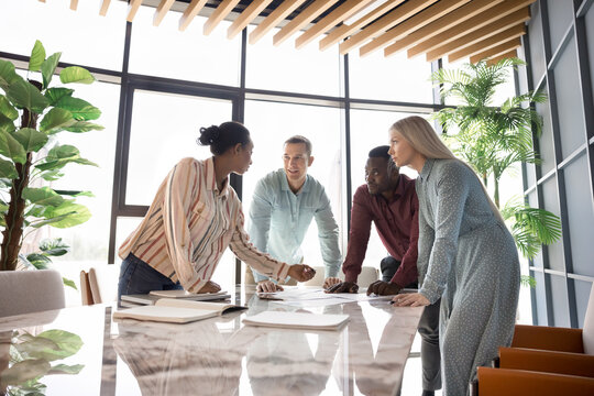 Professional team marketing department collaborating, working on presentation or project gathered together in modern meeting room, discussing ideas, planning strategy looking involved and motivated