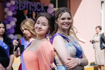 Female graduates smiling, embracing after commencement ceremony, celebrating academic success with mutual joy