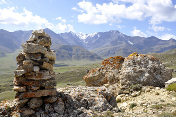 A stone tower on the mountainside to help travelers, shepherds, and tourists find their way. A tower built of mossy stones at the foot of snowy mountains