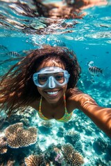 Fototapeta premium Many tropical fish swim next to her. Bright commercial style image. A attractive and sexy happy asian young woman with curly hair in a swimming mask and fins snorkeling among the corals.