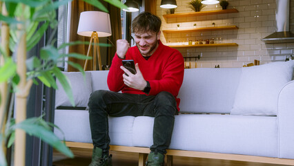 Excited Young Man Celebrating Victory While Looking at Smartphone, Happy Reaction to Online Success...