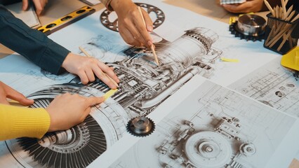 Engineers collaborate over detailed blueprints of an aircraft engine. The scene captures hands pointing to specific components, showcasing teamwork and innovation in design. SACTR