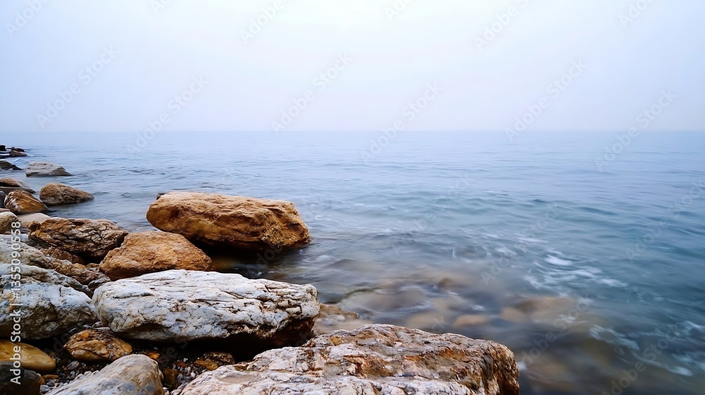 Poster serene rocky shoreline with gentle waves and calm water on a foggy day creating a peaceful atmospher