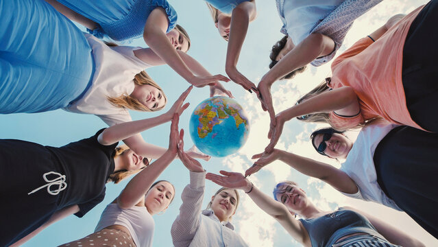 School friends making a circle with their hands around a small globe, symbolizing global unity and care for the environment