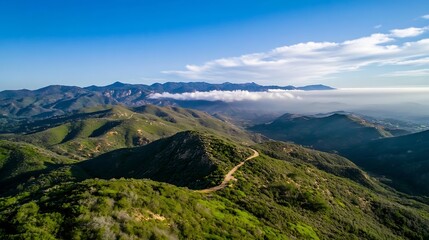 Obraz premium Breathtaking aerial view of lush green hills with a winding trail and mountains in the background : Generative AI