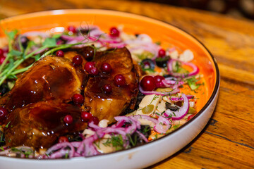 Braised pork with vegetables on a plate in a restaurant establishment on a wooden table. right side view