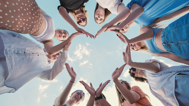 Students joining hands in heart shape to represent friendship, unity, and teamwork with blue sky background