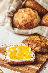 Half of a roll spread with cream cheese and lemon curd, variety of bread rolls in the background