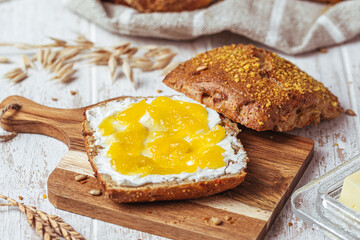 Half of a roll spread with cream cheese and lemon curd, variety of bread rolls in the background