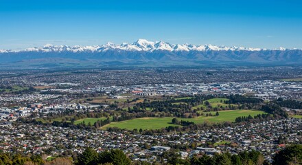 Scenic Cityscape with Mountain Range - Panoramic view of a city nestled against a majestic snow-capped mountain range under a clear blue sky