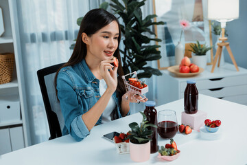 Smiling young beautiful Asian reviewing tasty mixed strawberry and cherry juice detox drinks,...