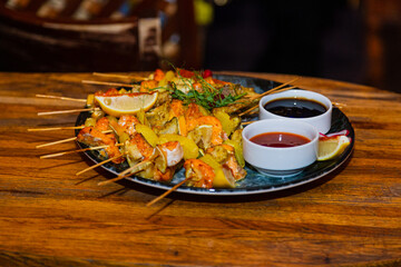 Shish kebab from seafood and red fish on wooden skewers on a plate with sauces on a wooden table. overall plan