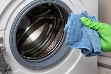 A woman's hand in a protective rubber glove holds a rag for a washing machine.