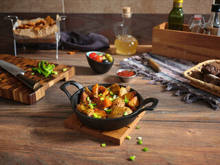 Cooked country-style potatoes in cast iron skillet on wooden table.