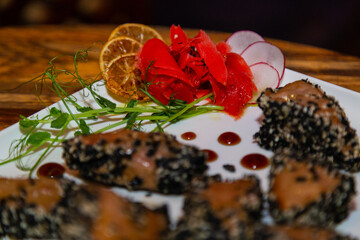 Grilled red fish meat with sesame seeds. A plate with fish and ginger on a wooden table in a restaurant. close-up of meat and ginger