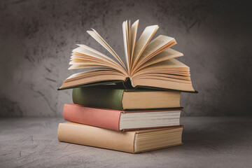 Stack of three books with one open book on top, showing pages, against a gray background, symbolizing education, knowledge, and reading