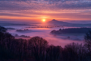 Obraz premium Vibrant sunrise over misty valleys with distant hills and dramatic clouds in the background