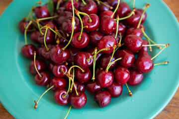 A vibrant pile of ripe red cherries sits on a teal plate, showcasing their juicy freshness