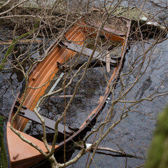 An abandoned boat partially submerged in a calm lake,creating a tranquil and moody atmosphere in a rural setting