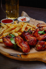 Appetizing fried wings with french fries sauce and beer on a wooden board. delicious food in the restaurant