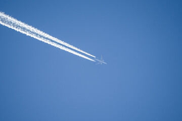 a twin engined jet liner aircraft in deep blue sky, contrails vapour trails