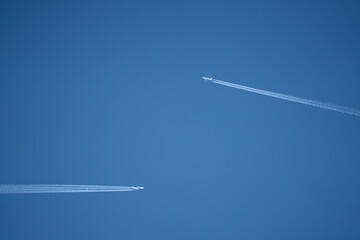 a pair of twin engined jet liner aircraft with contrails, passing at high altitude, clear blue sky