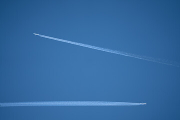 a pair of twin engined jet liner aircraft with contrails, passing at high altitude, clear blue sky