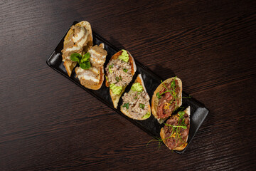 Three types of bruschetta on the table on a black plate beautiful serving in a restaurant. different fillings