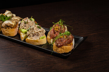 Three types of bruschetta on the table on a black plate beautiful serving in a restaurant. snack