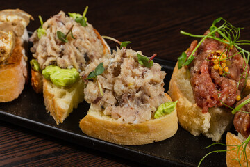 Three types of bruschetta on the table on a black plate beautiful serving in a restaurant. classic snack. close-up of fish bruschetta