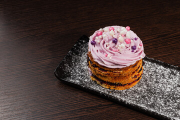 Appetizing fresh dessert cake on a black plate decorated with air cream and cake decorations sprinkled with powdered sugar. sweet dessert