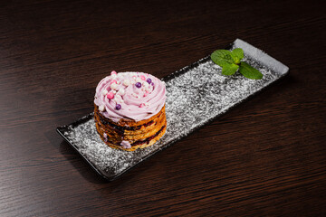 Appetizing fresh dessert cake on a black plate decorated with air cream and cake decorations sprinkled with powdered sugar. sweet dessert from the best confectioner in the city