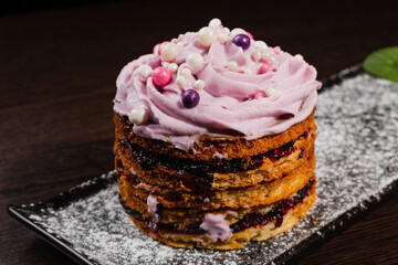 Appetizing fresh dessert cake on a black plate decorated with air cream and cake decorations sprinkled with powdered sugar. sweet dessert from the best confectioner in the city. close-up on the side