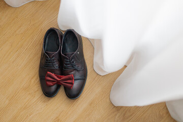 The groom's black shoes stand near the curtains on the floor with a butterfly on them wedding day. groom wedding details
