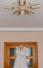 A beautiful white wedding dress hangs on a wooden door on the wedding day. visible chandelier