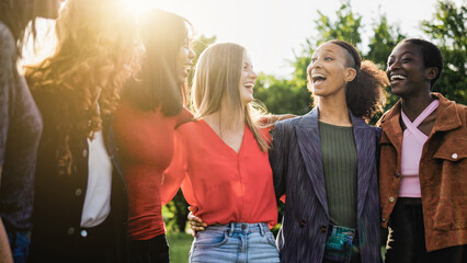 Group of women hugging each outside public park, Multiracial people celebrate together in summer...